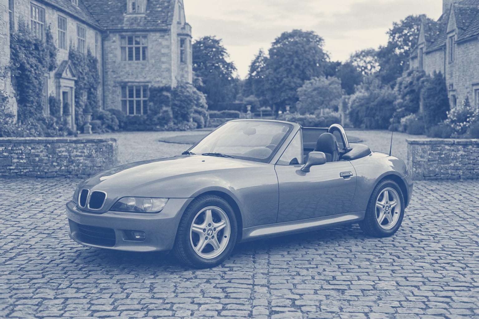 Klassischer BMW Z3 Roadster mit geöffnetem Verdeck vor einem ruhigen historischen Gutshof im warmen Nachmittagslicht.