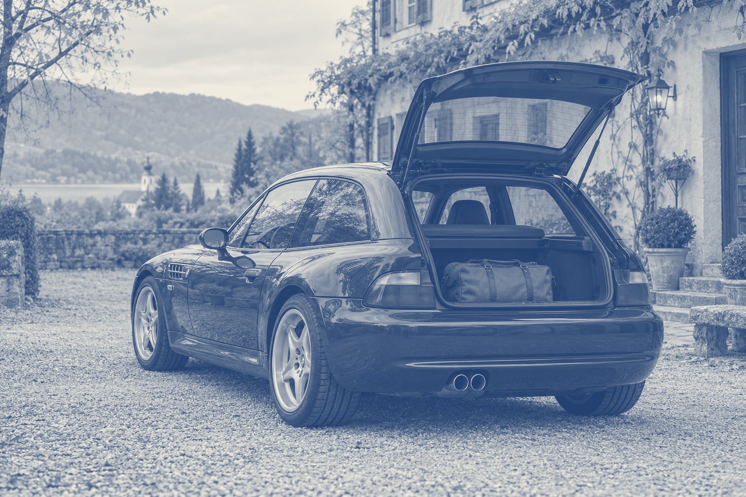 Dunkelblaues BMW Z3 Coupé mit geöffneter Heckklappe und einer weichen Reisetasche in einer ruhigen süddeutschen Hofszene.